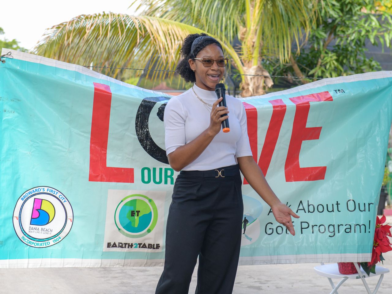 A speaker with a microphone in front of the Love Our Nation golf program banner