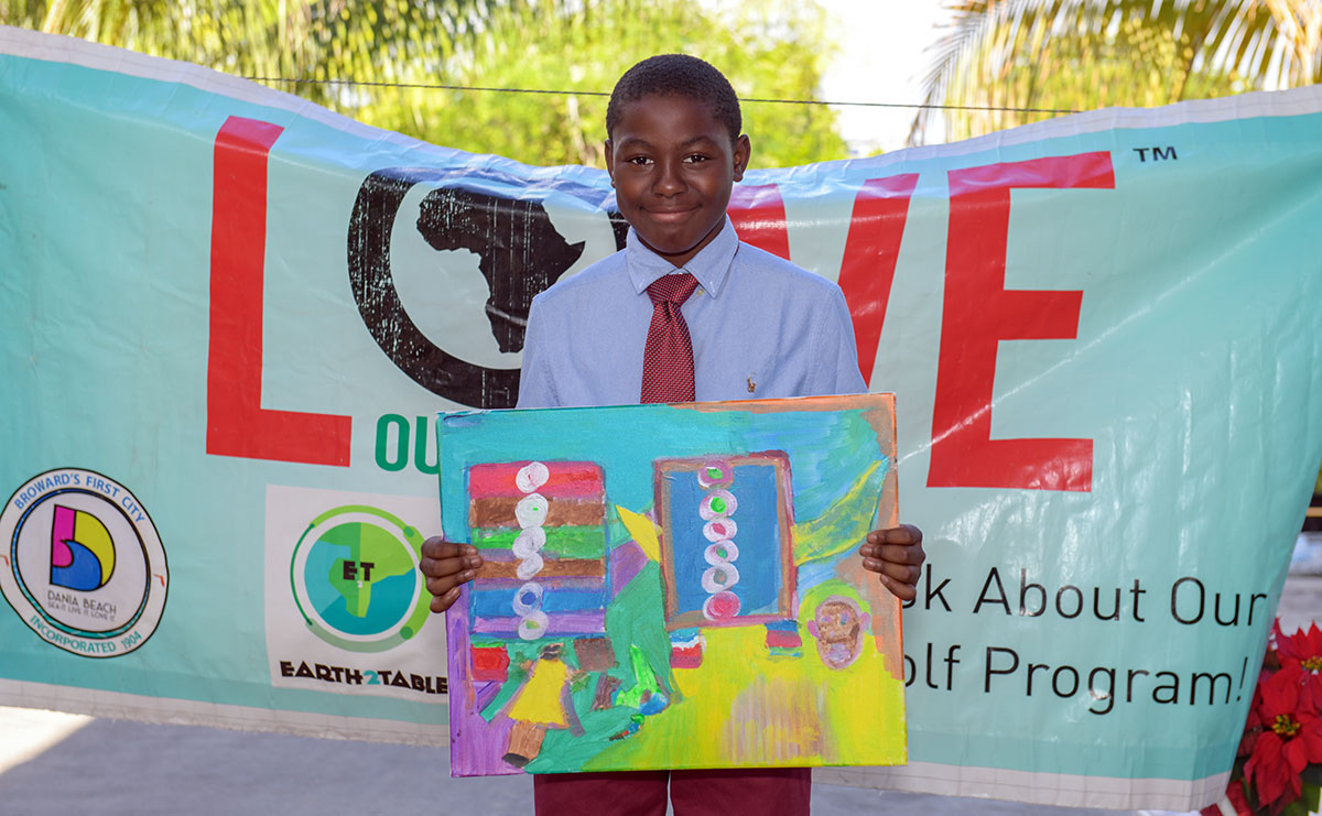 Student holding his colorful painting in front of the Love Our Nation banner