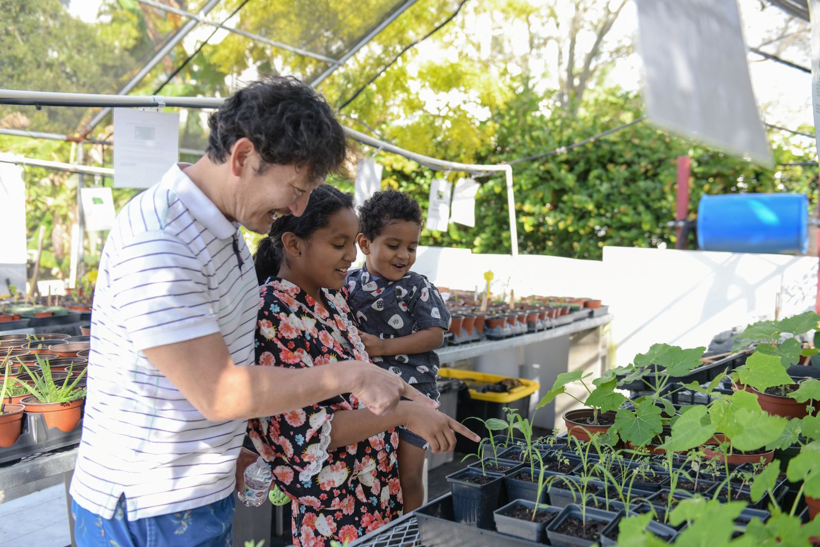 A mentor showing a mother and her children seedlings inside the greenhouse