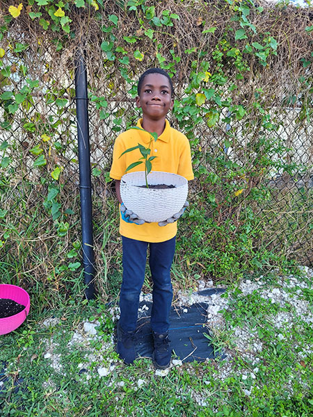 Student proudly holding a potted seedling he planted
