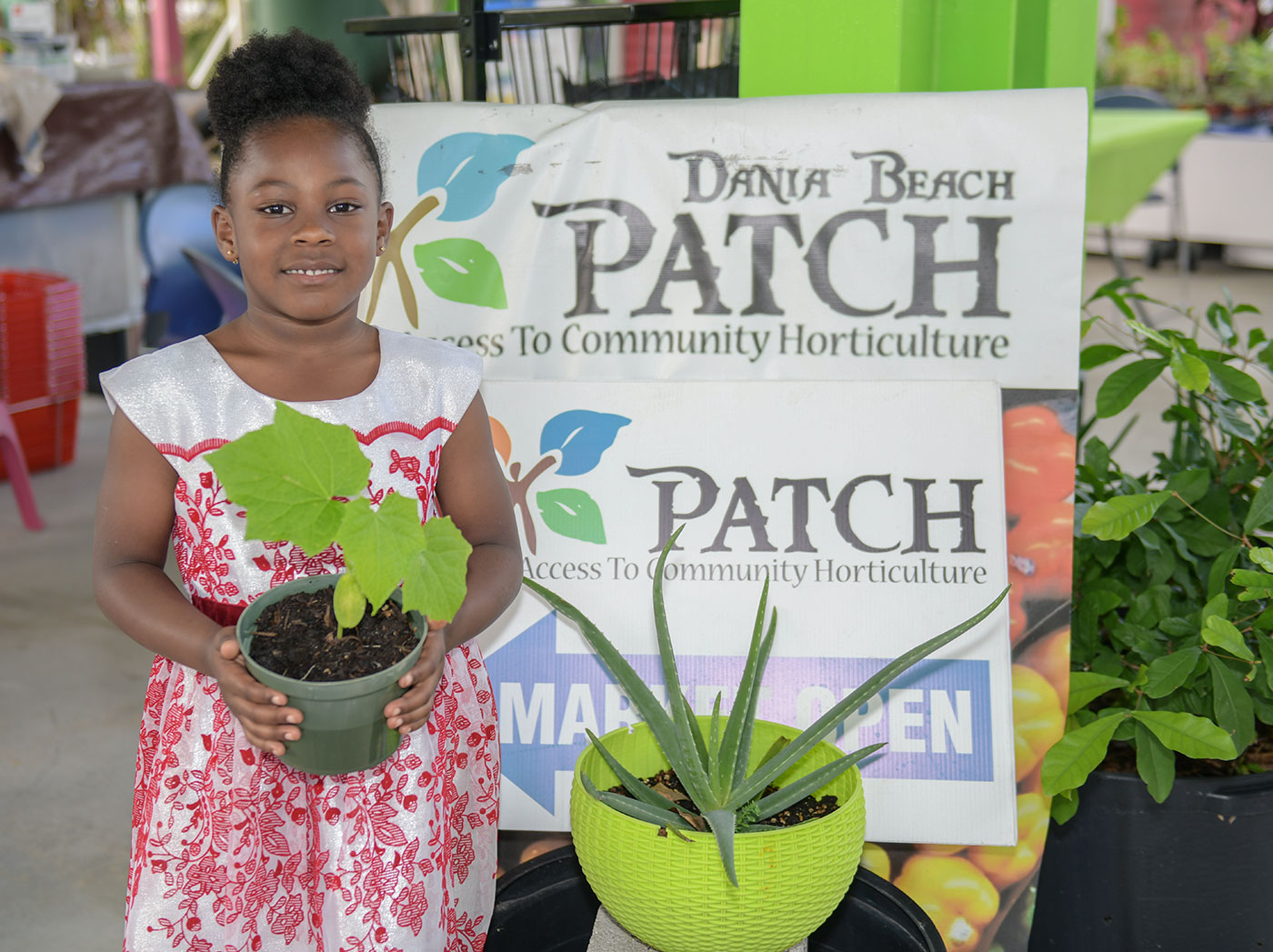 A young student holding a potted plant at the Dania Beach PATCH market